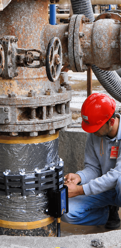 Technician installing a HydroFLOW unit on a stainless steel pipeline